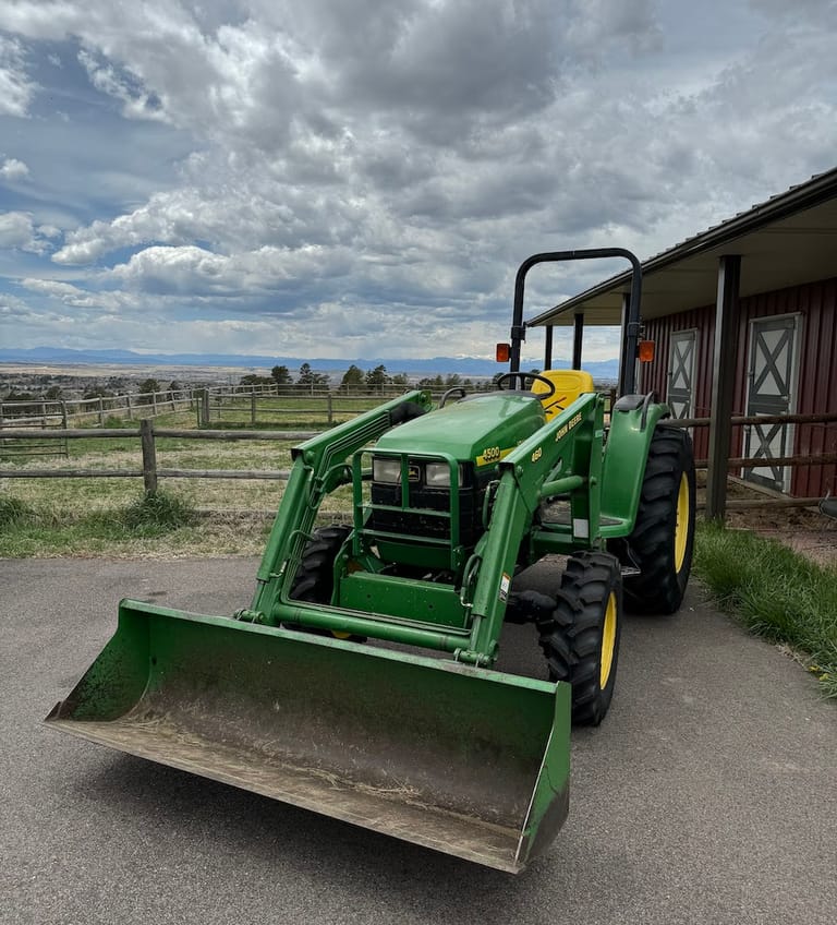 The John Deere tractor with its loader, parked by the red barn